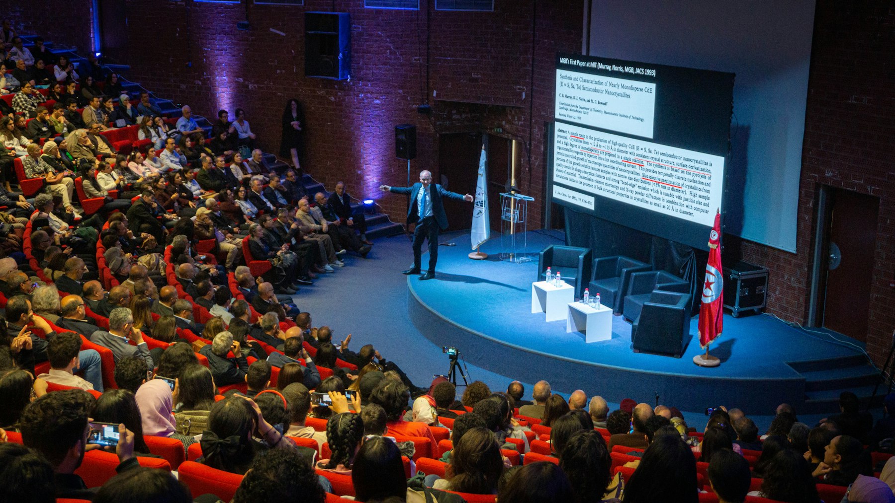 A speaker addressing a full auditorium at a community summit