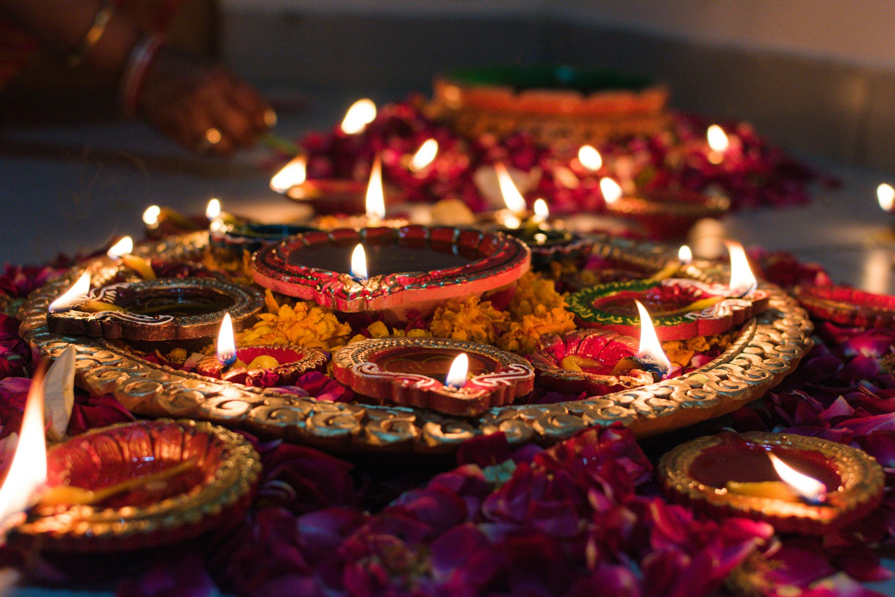 Lit clay oil lamps arranged on a tray with scattered flower petals